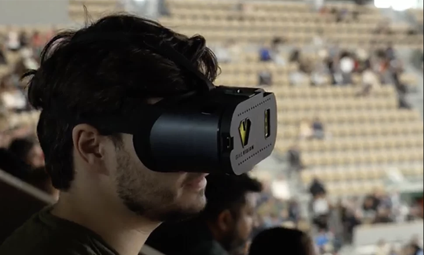 Photographie d'un homme portant un casque basse vision. Au second plan on distingue les gradins d'un stade.